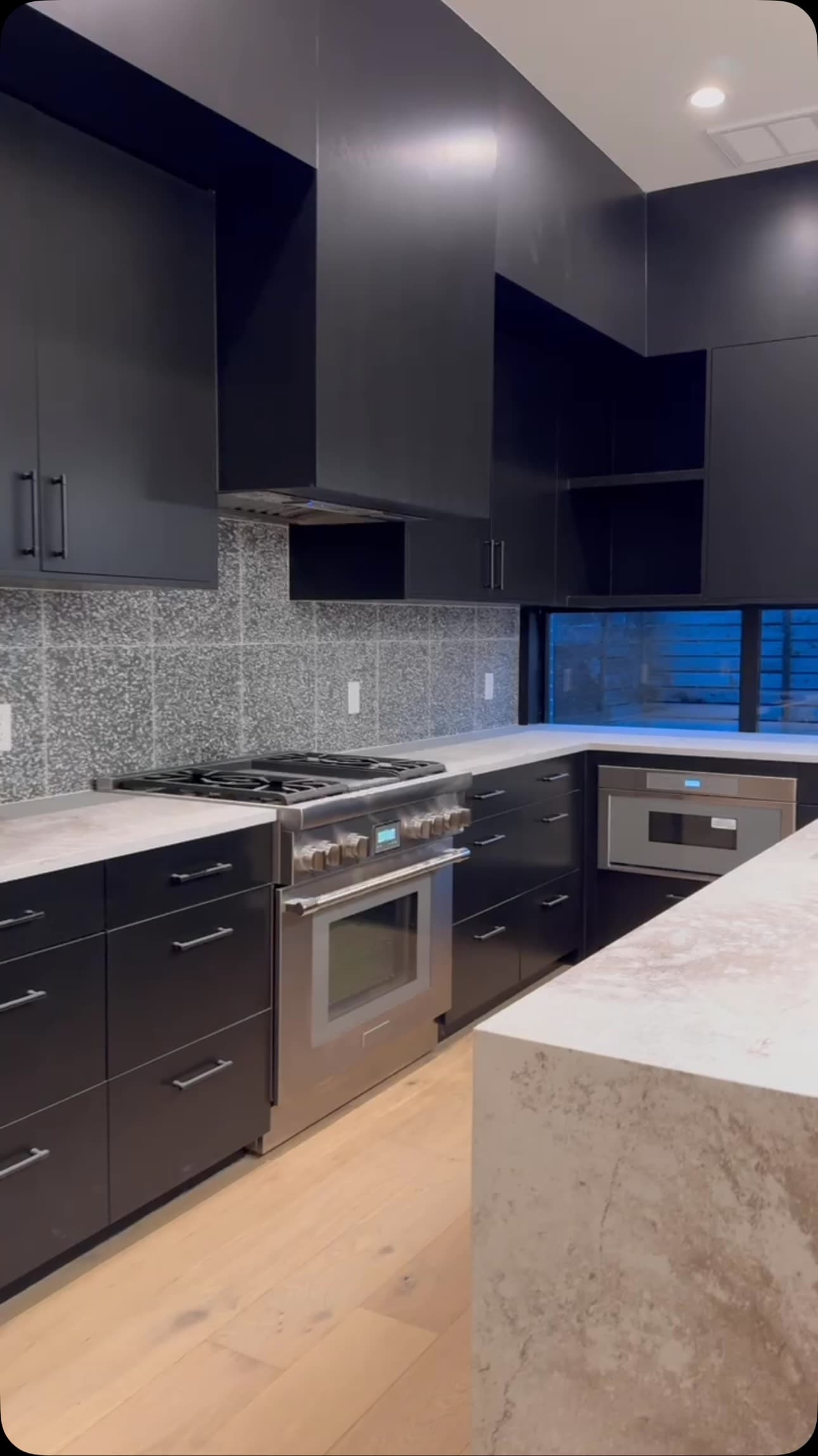 Finished New Life kitchen with full-height dark cabinetry and a pale stone waterfall island