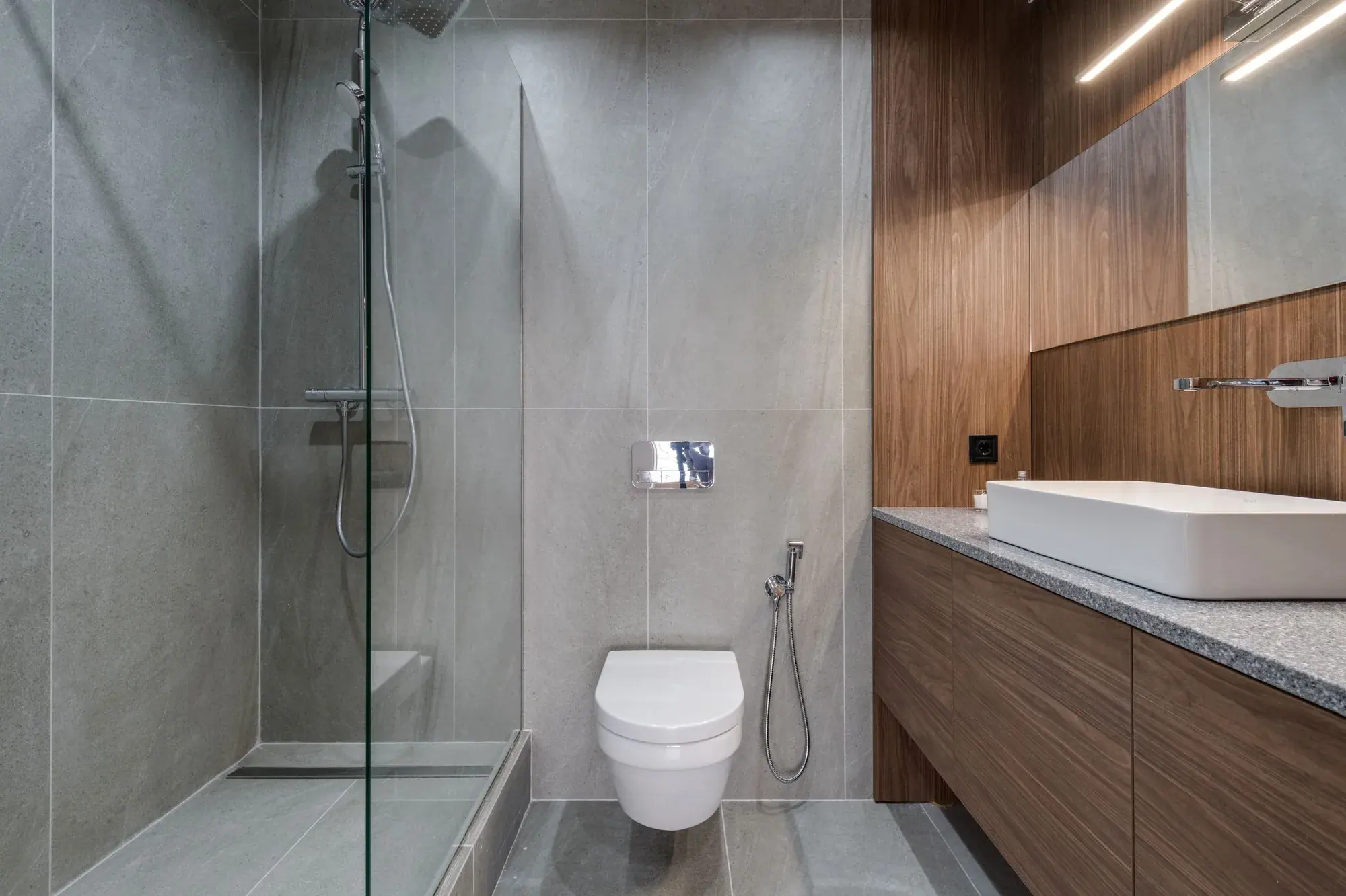 Compact bathroom design inspiration with a glass shower, gray tile, toilet, and wood vanity