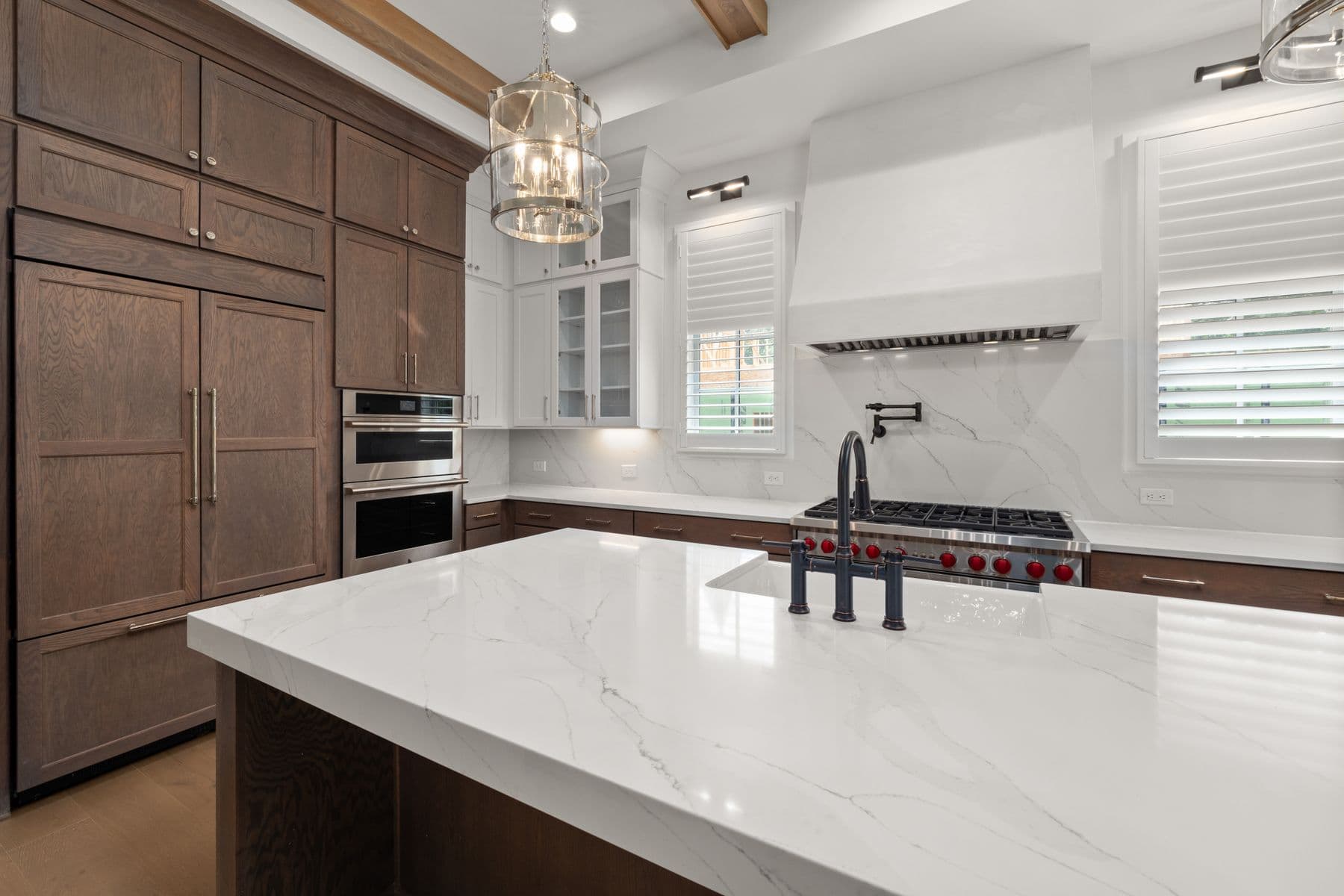 High-end kitchen inspiration with a large marble island, dark wood cabinetry, a professional range, and layered lighting