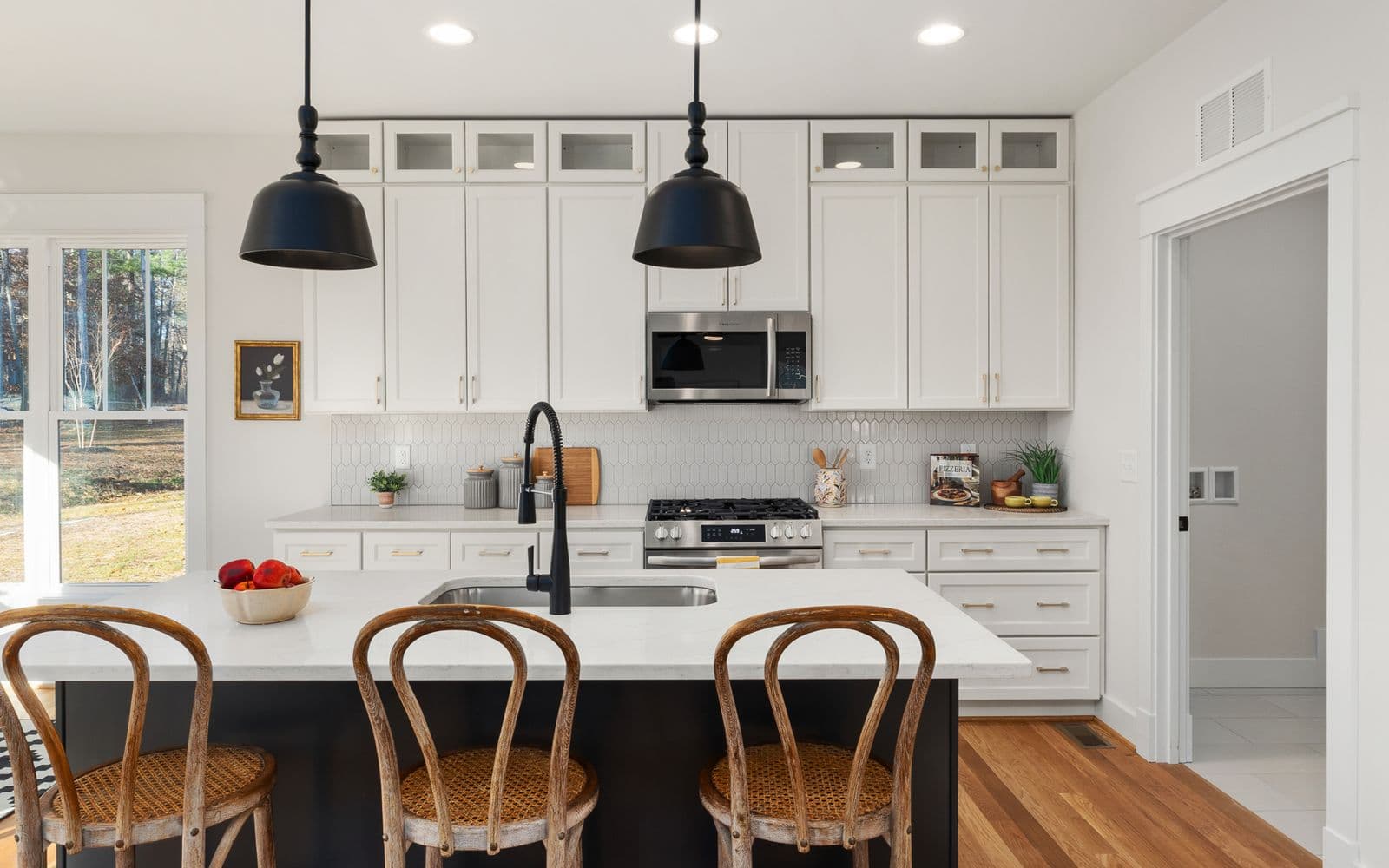Bright kitchen inspiration with white cabinetry, a black island, wood seating, and large windows